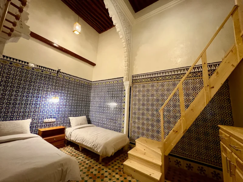 Triple Room at Ilyana Surf House in Rabat featuring patterned blue and earth-tone zellige tiles, wooden furnishings, and loft bed access.