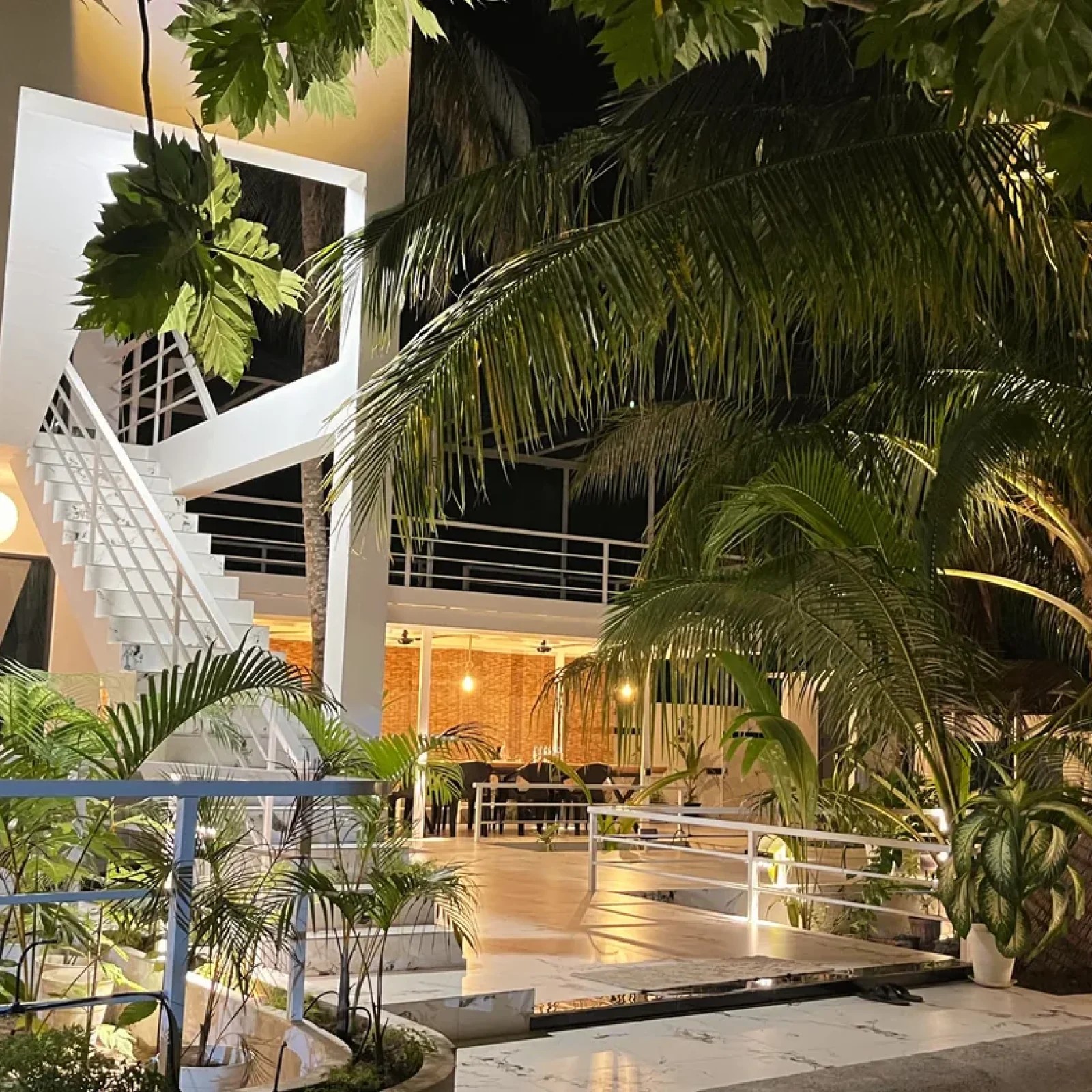 Terrasse moderne à l'Oceana Inn Maldives avec escalier en colimaçon, plantes tropicales luxuriantes et architecture contemporaine sous un éclairage chaleureux du soir.