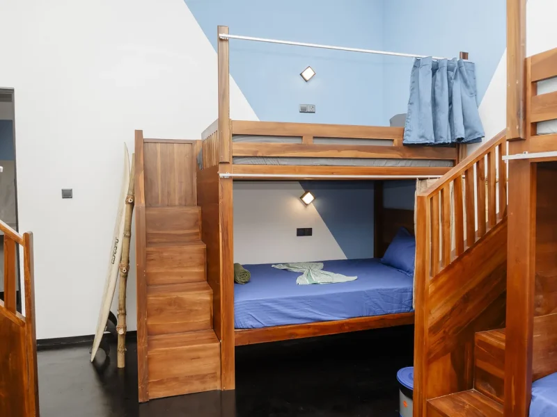 Hölzernes Etagenbett mit blauer Bettwäsche in einem Schlafsaal mit weißen und blauen Wänden im Wanderlust Surf Camp.