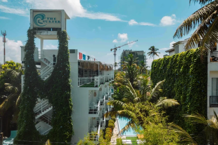 La torre de señalización de The Surfer Beach Camp con pilares cubiertos de hiedra domina los edificios blancos de varias plantas, la piscina y la vegetación tropical de la propiedad en Weligama.