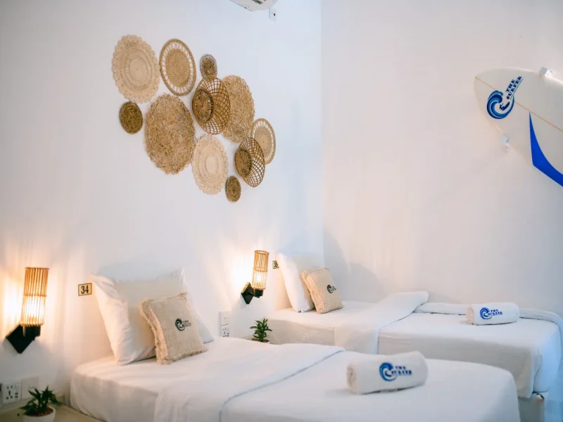 Mixed dorm room at The Surfer Beach Camp with white beds, woven wall decorations, and beige cushions in Weligama.
