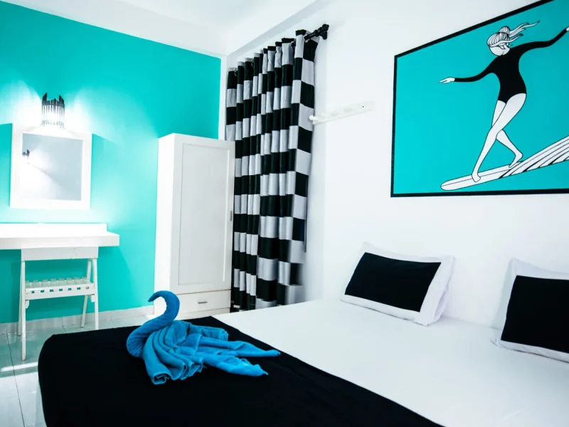 Weligama Surf Camp private single room with turquoise walls, black and white patterned curtains, and surfboard artwork.