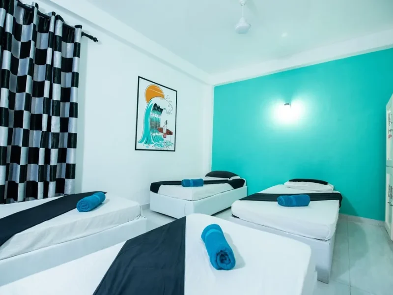 Mixed dorm bedroom at TS2 Weligama Surf Camp featuring white beds, turquoise accent wall, and surf-themed wall art.