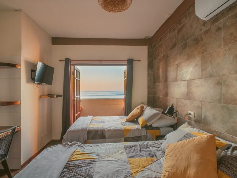 Chambre Double Suite à AST Surf Hotel à Punta Roca avec lits jumeaux et vue océan à travers les portes vitrées.