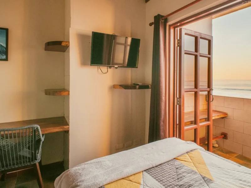 Chambre avec lit, TV murale à cadre vert, étagères en bois et portes vitrées s'ouvrant sur la terrasse.