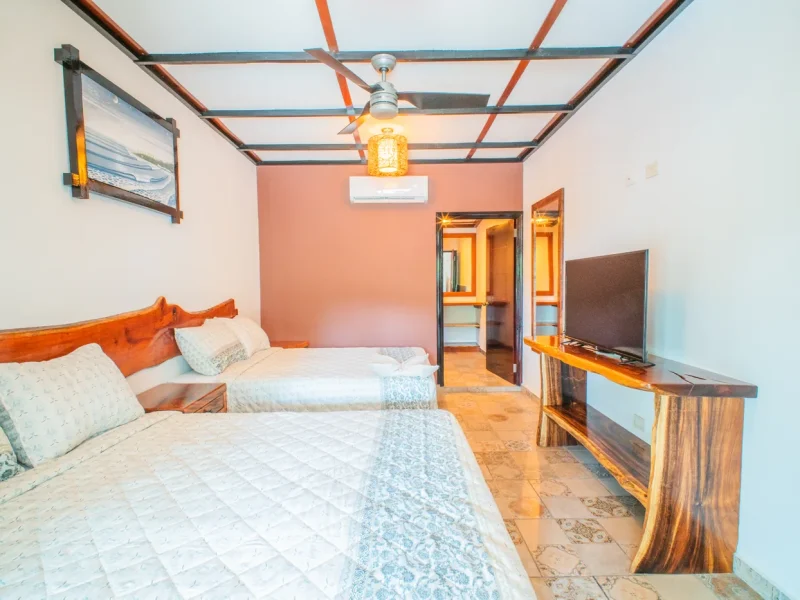 Dormitorio de la Double Poolside Suite con camas gemelas, pared de acento naranja, techo con vigas, TV y puertas en suite en Casa Las Flores.