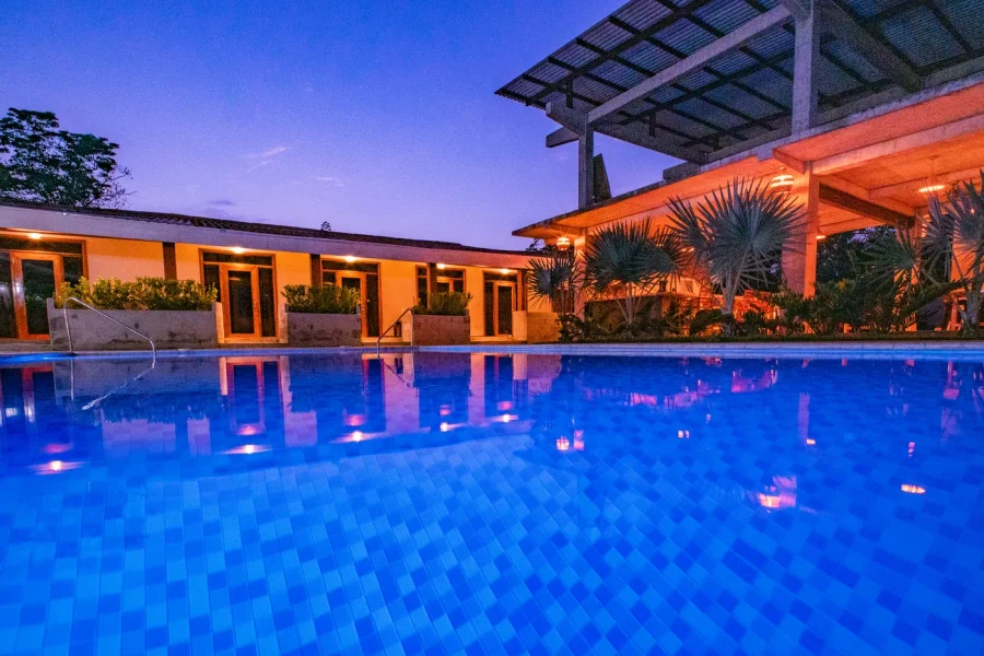 Piscine de Casa Las Flores avec éclairage sous-marin bleu et structures de terrasse illuminées en orange au crépuscule à Las Flores, El Salvador.