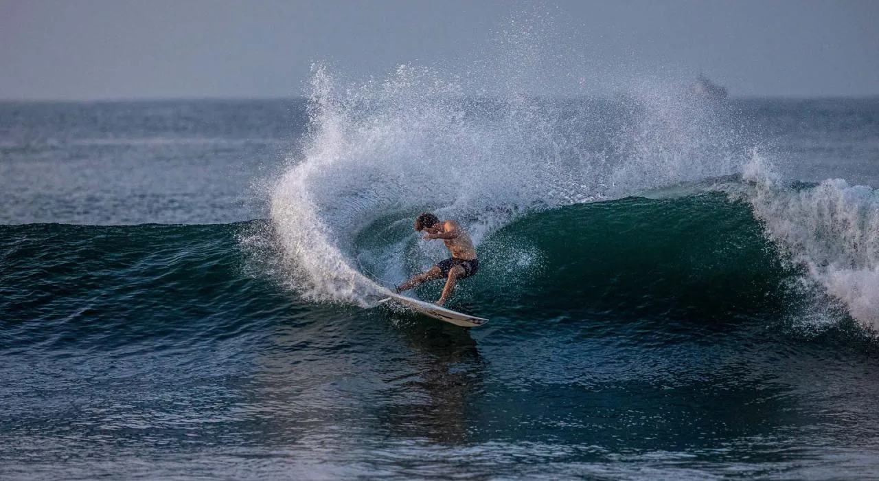 Shirtless male surfer riding a glassy green wave at Punta Roca with white spray.
