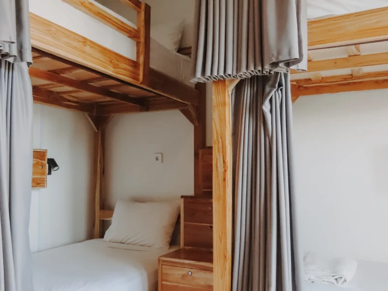 Wooden bunk bed setup in shared dorm room with gray linen curtains and white bedding at Elsewhere Surf Camp Bali.