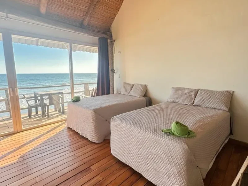 Triple Suite bedroom at Punta Mango Surf Resort featuring two beds with sea view through glass doors opening to terrace.