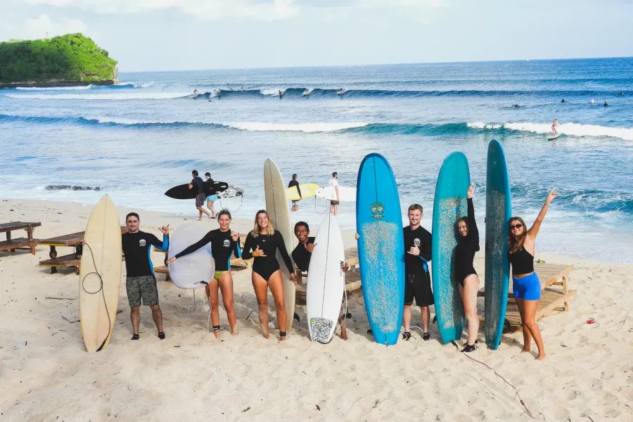 Ten surfers hold their boards while posing on the sand at Canggu beach with active waves visible in background.