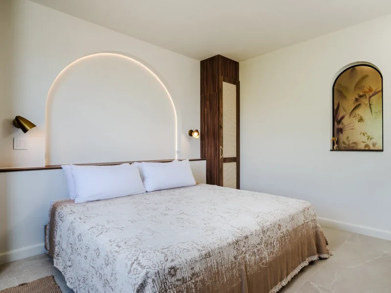 Standard King bedroom with neon-lit arched headboard, light blue pillows, patterned bedding, and dark wood wardrobe at Iguana Surf Boutique Hotel in Tamarindo.