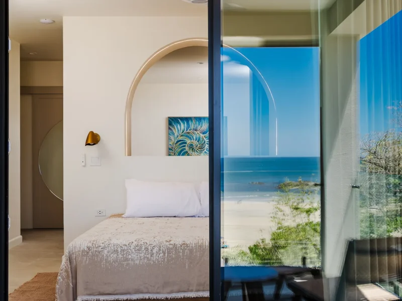 Presidential Suite bedroom at Iguana Surf Boutique Hotel in Tamarindo, Costa Rica with ocean and beach view through glass door.